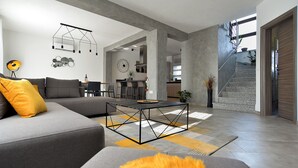 Un salon moderne avec un canapé gris, une table basse et un escalier menant à l’étage supérieur.