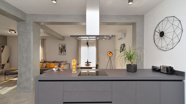 Une cuisine moderne dotée d’un îlot central, de luminaires suspendus et d’une œuvre d’art géométrique ornant un mur.
