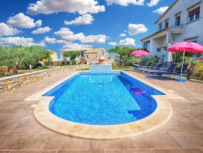 A rectangular swimming pool with a mosaic tile design, surrounded by a stone wall and a tiled deck.