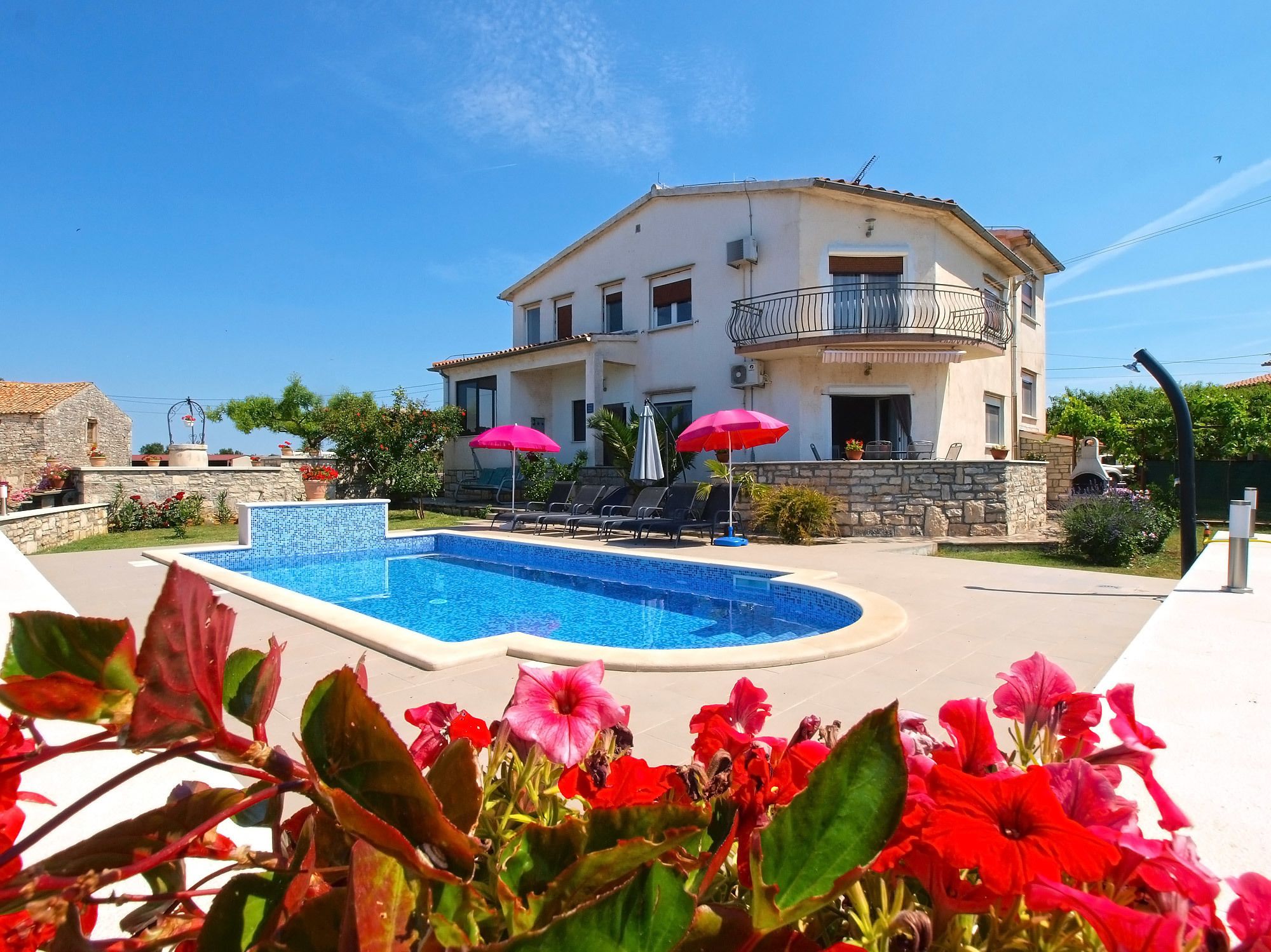A two-story building with a swimming pool, outdoor seating, and a stone wall.