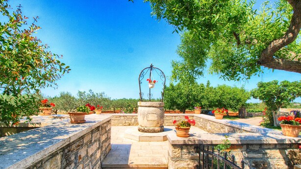 A stone staircase leading up to a fountain with a metal arch, surrounded by potted plants and trees. - Apartment 1386 (Vodnjan)