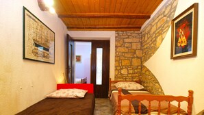 A bedroom with two single beds, a wooden ceiling, stone walls, and a door leading to another room. - Apartment 1388 (Vodnjan)