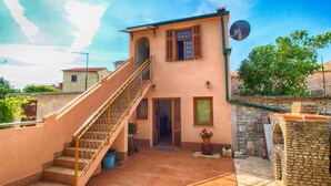 A two-story building with a staircase leading to the entrance, a satellite dish, and a stone wall. - Apartment 1388 (Vodnjan)