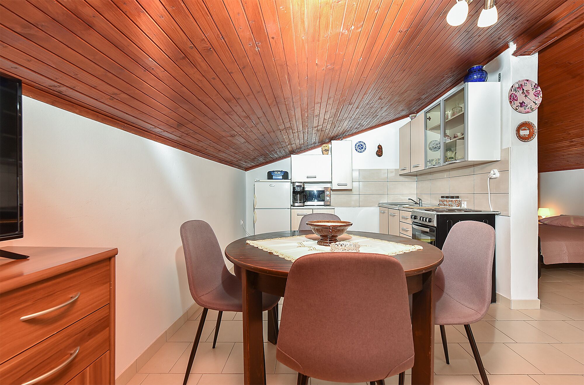 A dining area with a round table, four chairs, and a wooden ceiling.