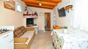 Une pièce chaleureuse avec un plafond en bois, une cheminée, un canapé, une table recouverte d’une nappe à motifs floraux et un téléviseur fixé au mur.