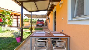 Une terrasse extérieure avec une table et des chaises, un espace abrité et une voiture garée en arrière-plan.