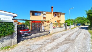 Une maison à deux étages avec une voiture rouge garée devant, une allée en gravier et un ciel bleu dégagé.