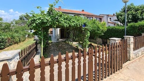 Una propiedad residencial con camino de entrada pavimentado, valla de madera y jardín con vegetación.
