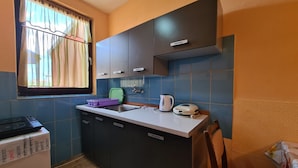 Una cocina compacta con armarios oscuros, un lavamanos, una tetera y un tostador.