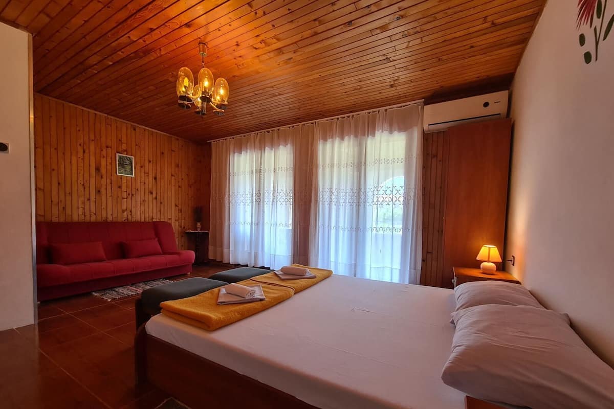 A wooden-paneled room with a bed, a red sofa, and a small table with a lamp.