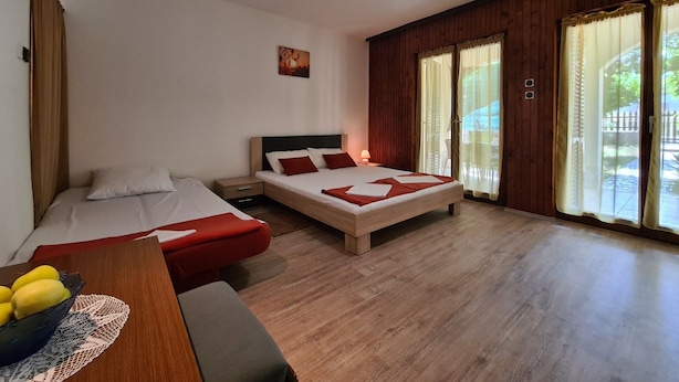 Un dormitorio con dos camas, suelo de madera, un escritorio con un cuenco de fruta y una ventana con cortinas.