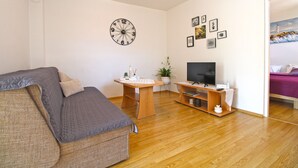 Una sala de estar con un sofá, un televisor sobre un mueble de madera, un reloj de pared y varias fotografías enmarcadas.