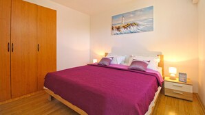 Un dormitorio con un armario de madera, una cama con colcha morada, una mesita de noche con lámpara y un cuadro de un faro en la pared.
