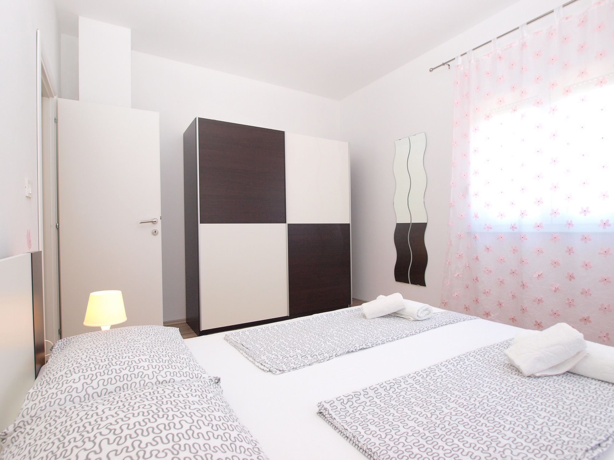 Una camera d'albergo con un letto, comodini, un armadio e una finestra con tende floreali.