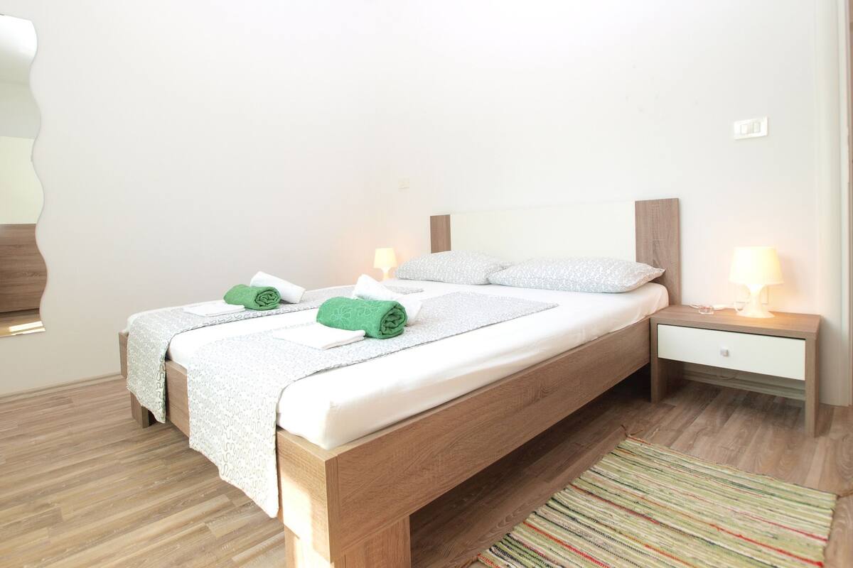 A neatly made bed with a wooden headboard, two bedside tables with lamps, and a striped rug on a wooden floor.