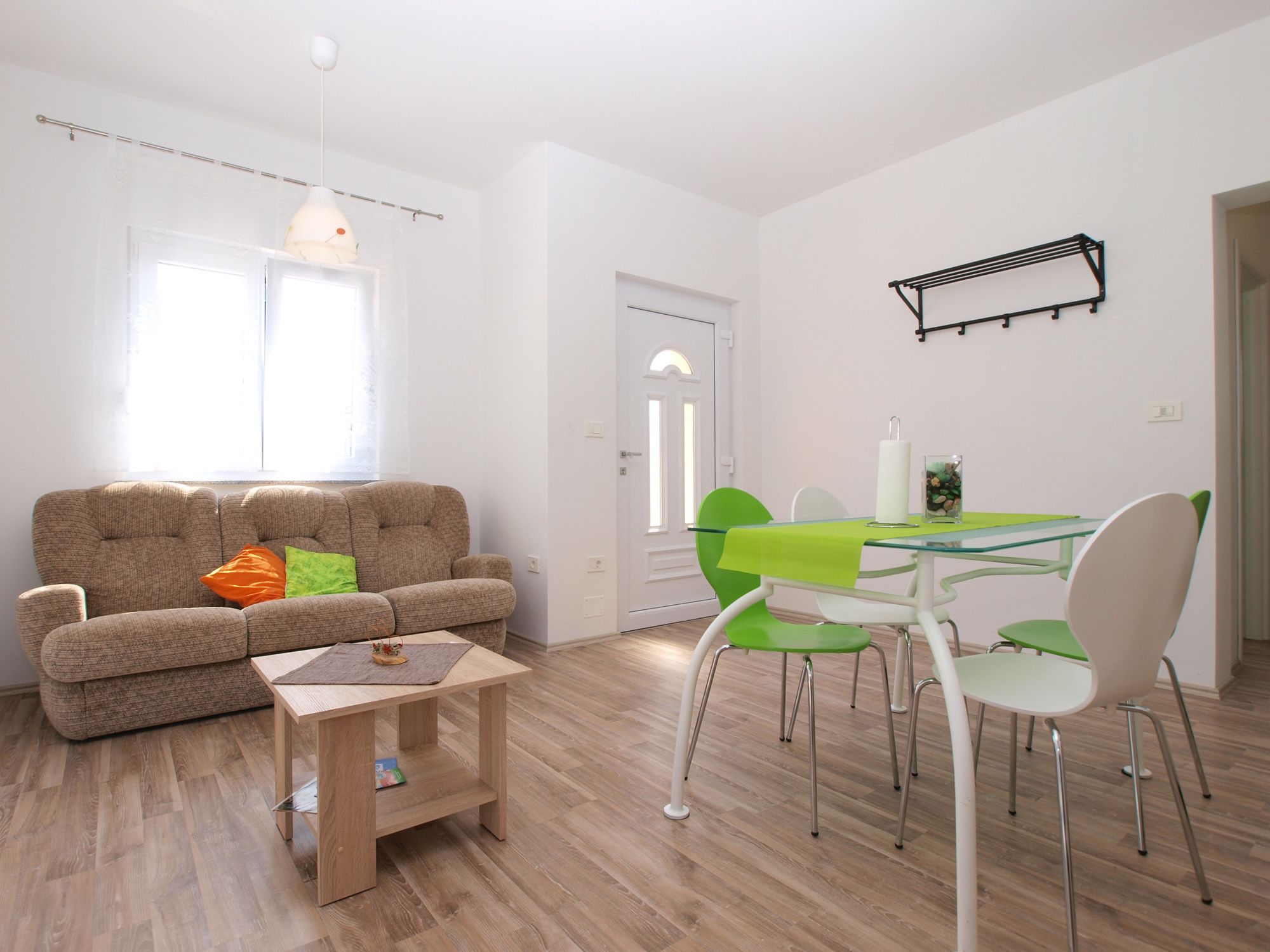A living room with a sofa, a small table, and a dining area with chairs and a glass table.
