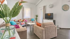 A modern living room with a sofa, armchairs, a coffee table, and a TV. There is a large window with curtains, a clock on the wall, and a plant in the corner. - Villa 1404 (Zminj)