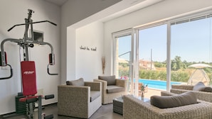 A spacious room with a gym area, wicker furniture, and a large sliding glass door leading to a pool. - Villa 1404 (Zminj)