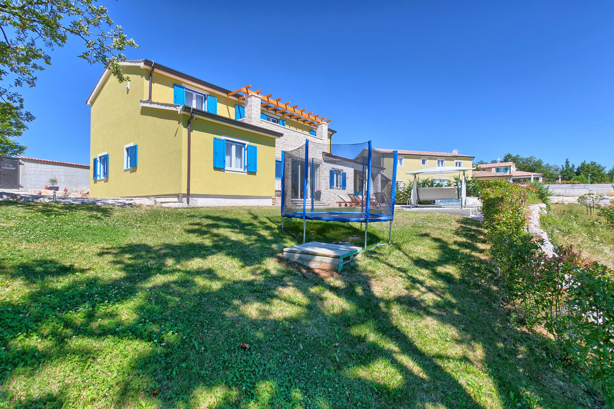 A residential property with a trampoline in the yard, a yellow building with blue shutters, and a stone chimney.