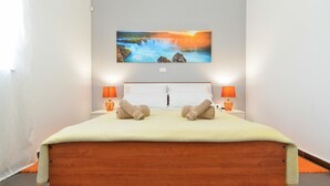Un dormitorio con cama, dos lámparas de noche, un cuadro de una cascada y vistas al exterior.