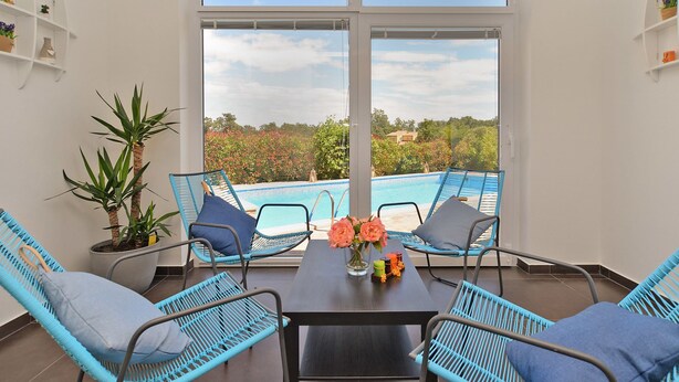 Un balcón con vista a la piscina, sillas de mimbre y una mesa con flores.