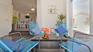 Comedor con sillas de mimbre azules, una mesa con velas y vistas al exterior.
