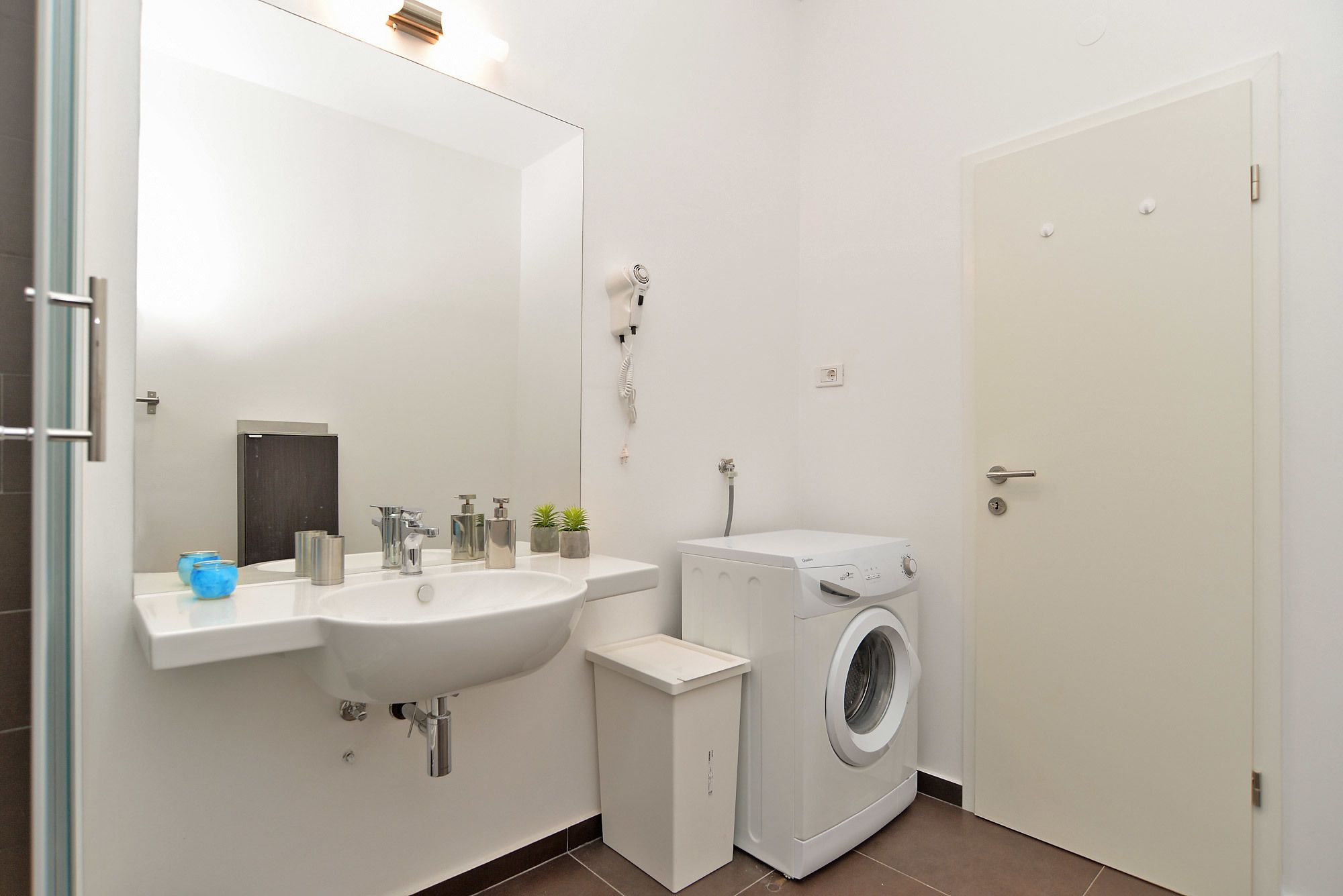 Ein kleines Badezimmer mit Waschbecken, Spiegel und einer Frontlader-Waschmaschine.