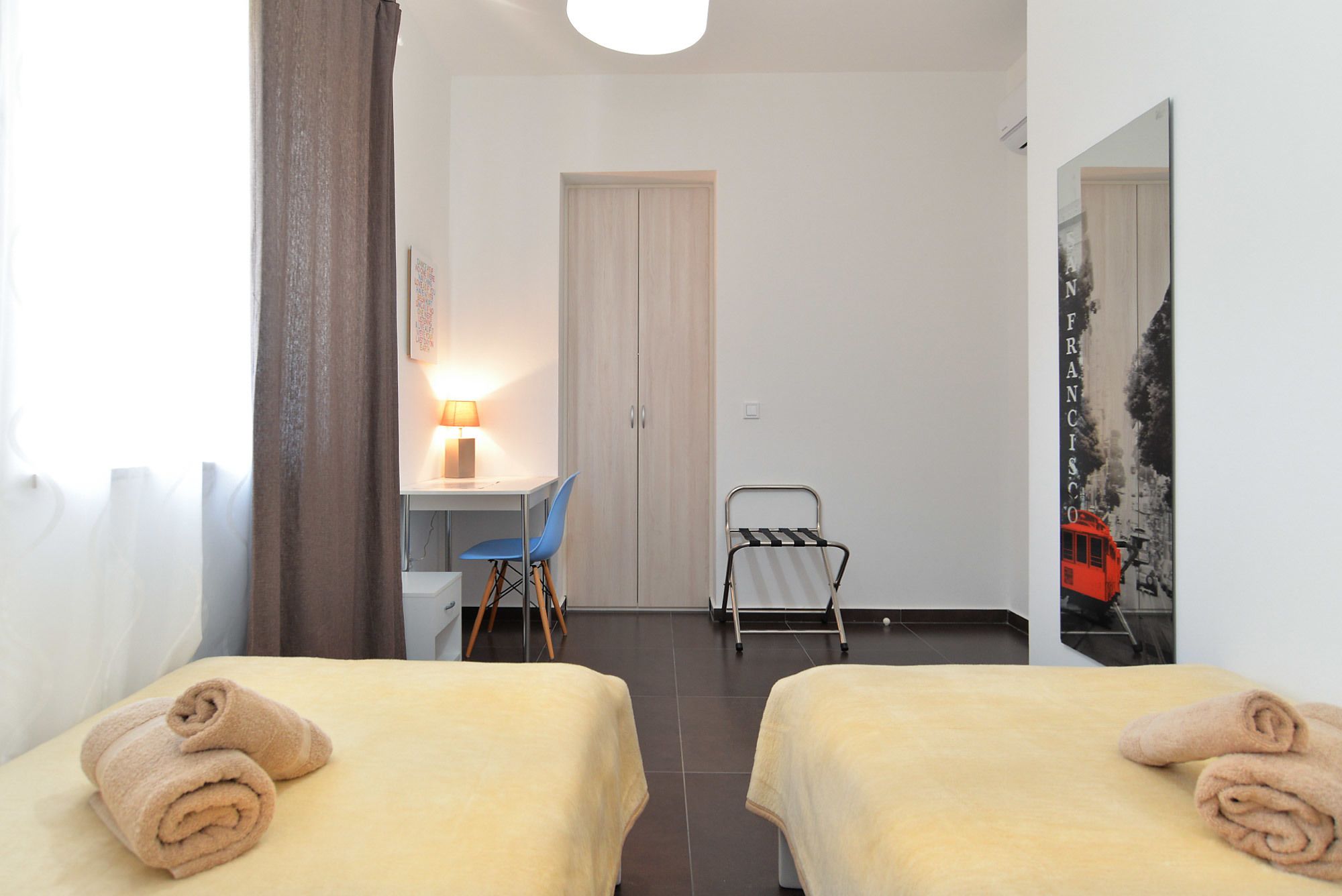 A hotel room with two beds, a desk with a chair, a radiator, and a mirror on the wall.