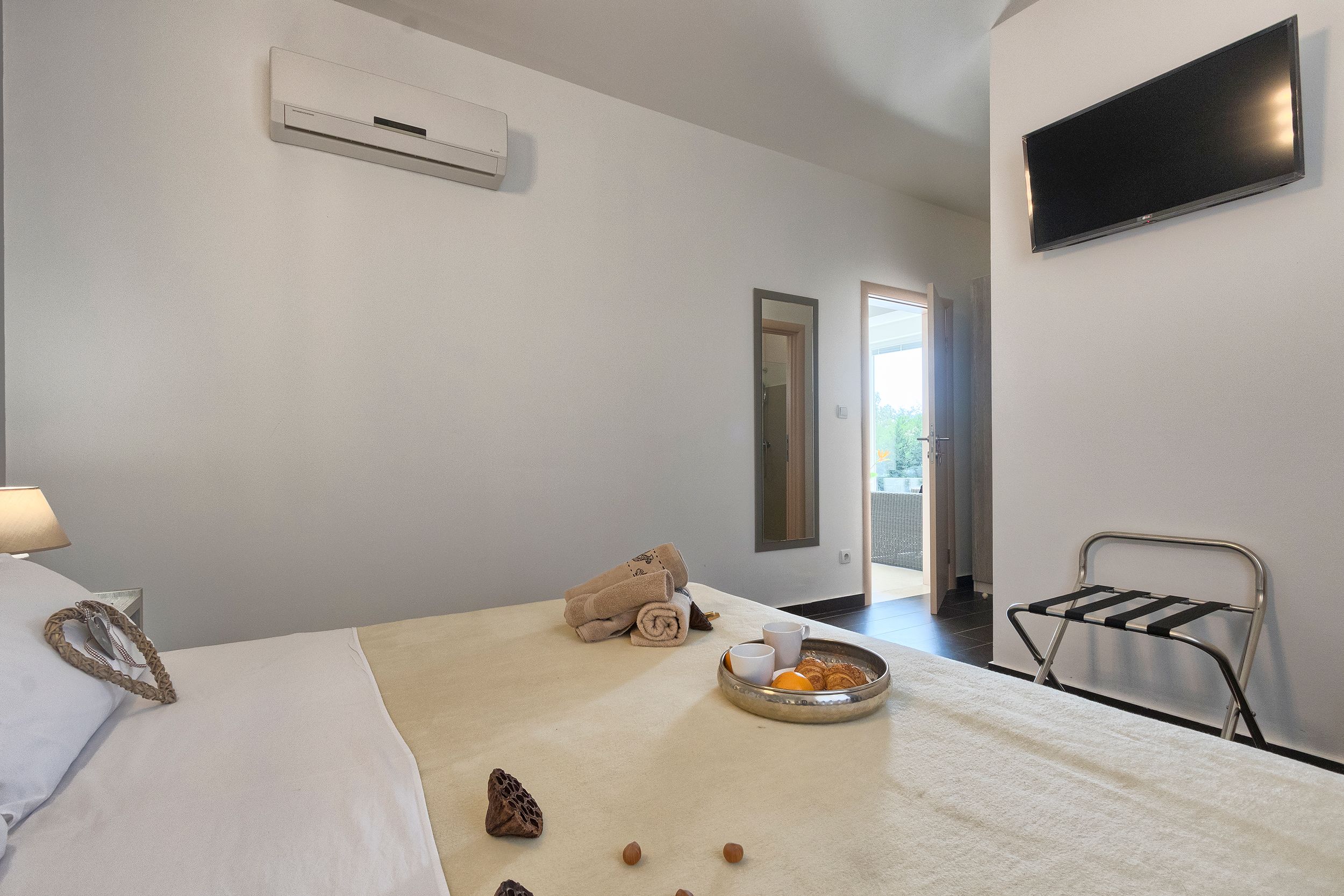 A hotel room with a bed, a tray with cups and pastries, towels, and a TV mounted on the wall.