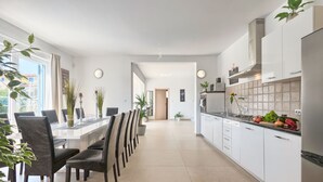 Eine moderne Küche mit weißen Schränken, ein Essbereich mit schwarzen Stühlen und Blick ins Freie.