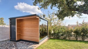 A modern outdoor sauna with a wooden exterior and glass walls, surrounded by a well-maintained garden and a clear sky. - Villa 1521 (Zminj)