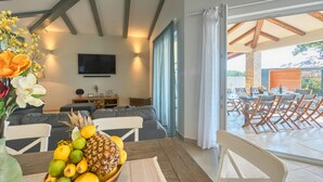 A modern living room with a sofa, a dining table with fruit, a TV, and a view to an outdoor patio. - Villa 1521 (Zminj)