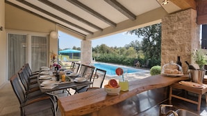 A covered outdoor dining area with a pool view, stone pillars, and a wooden bar. - Villa 1522 (Zminj)