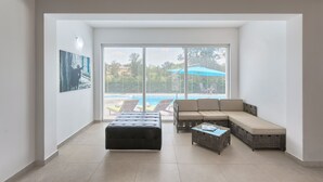 A spacious living area with a large window, a sectional sofa, a black ottoman, and a wicker coffee table. - Villa 1522 (Zminj)