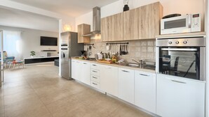 A modern kitchen with white cabinets, a built-in microwave, an oven, and a central island with a sink and various kitchen utensils. - Villa 1522 (Zminj)