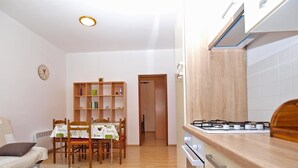 A modern kitchen with a gas stove, wooden cabinets, and a dining area with a table and chairs. - Apartment 1407 (Fazana)