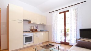 A compact living space with a kitchenette, a glass coffee table, and a TV in a living area. - Apartment 1407 (Fazana)