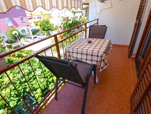 A balcony with a checkered table and two chairs, surrounded by a metal railing and potted plants. - Apartment 1407 (Fazana)