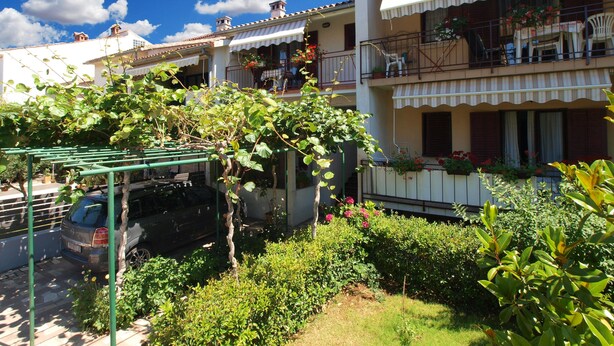 A residential building with multiple balconies, a garden area with potted plants, and a parked car. - Apartment 1407 (Fazana)