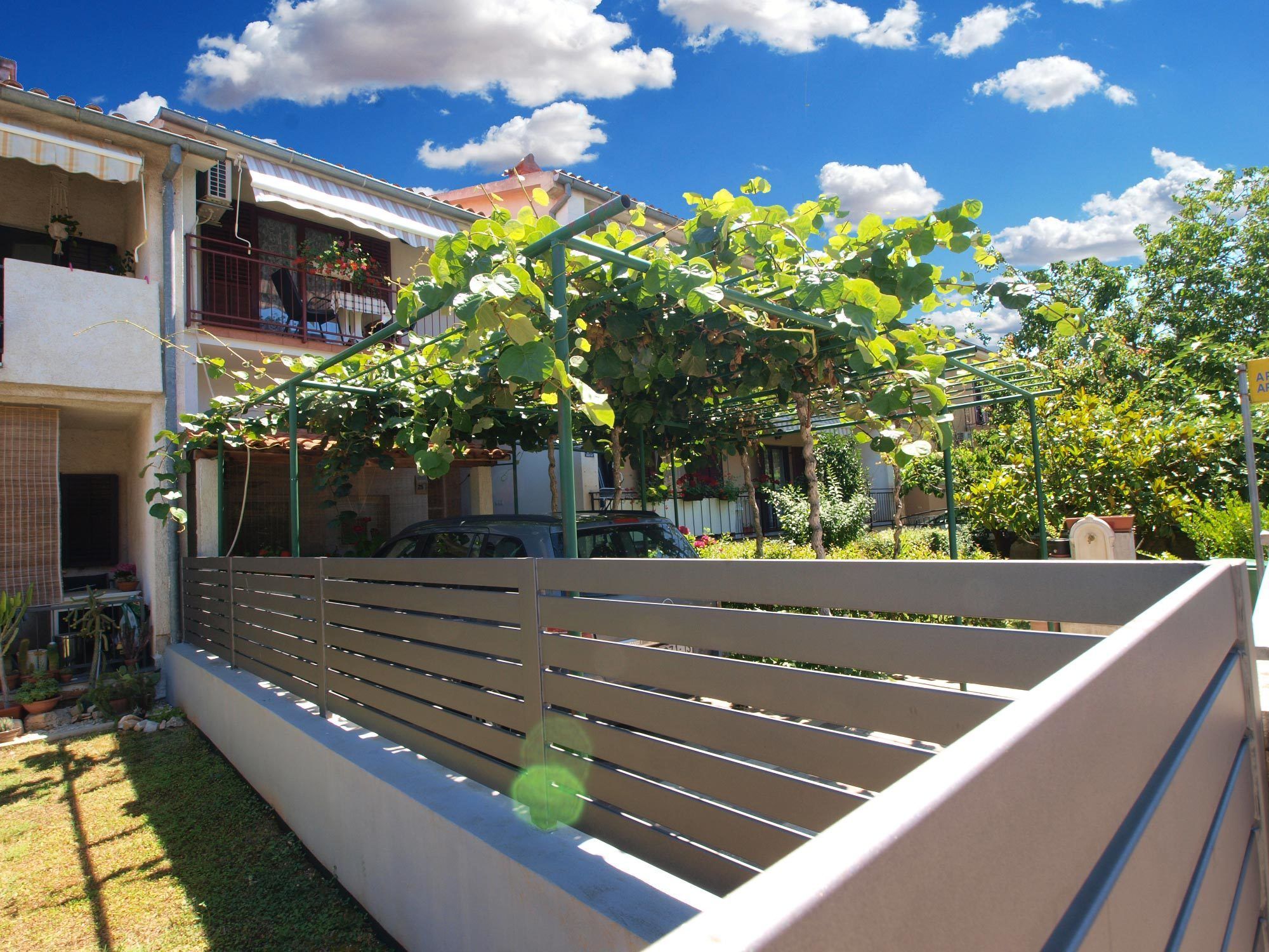 A residential area with a white fence, a parked car, and a building with a balcony.