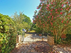 A stone-paved entrance with a metal gate, surrounded by lush greenery and flowering trees. - Apartment 1410 (Medulin)