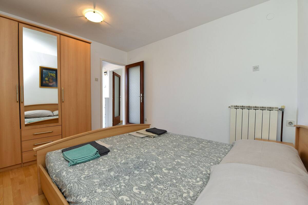 A bedroom with a bed, a wardrobe, a radiator, and a door leading to another room.