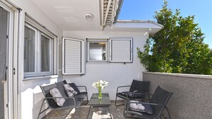 Een balkon met twee zwarte stoelen, een tafeltje en een vaas witte bloemen.