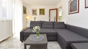 Een moderne woonkamer met een grijze modulaire bank, een klein tafeltje met een bloevas, en kunstwerken in lijsten aan de muren.