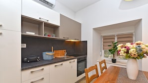 A modern kitchen with white cabinets, a wooden dining table, and a vase of flowers. - House 1411 (Marcana)