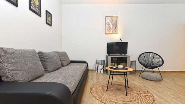A living room with a sofa, a TV, a chair, and a small table with a rug. - House 1411 (Marcana)