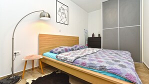 A bedroom with a wooden bed, a floor lamp, a cowhide rug, and a large grey sliding door. - House 1411 (Marcana)