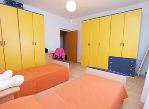 Quarto com duas camas, armários amarelos, uma escrivaninha com tecido rosa e uma porta de madeira.