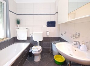 Casa de banho moderna com banheira, sanita, lavatório e uma pequena tigela verde e amarela.