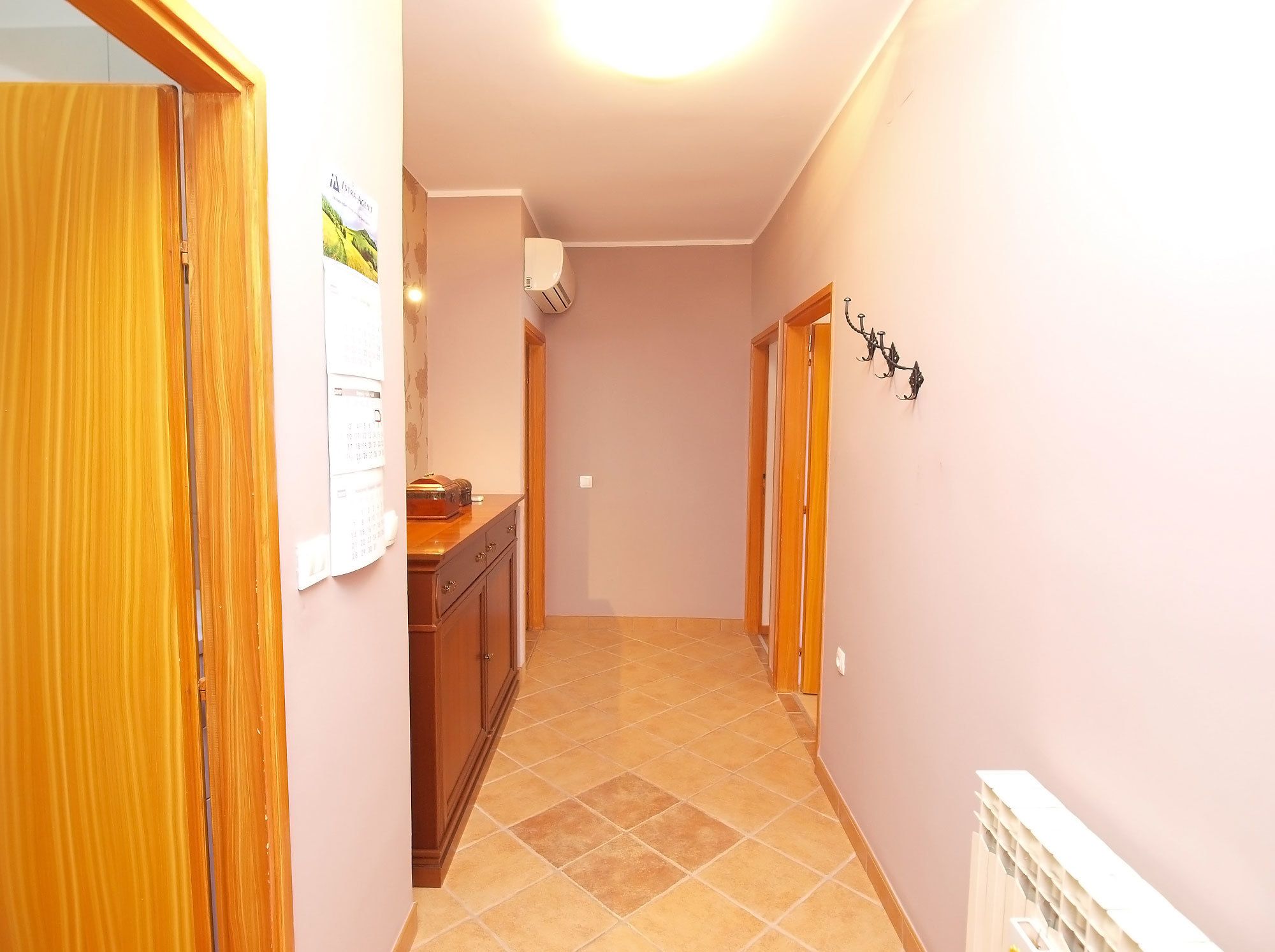 Un pasillo con una puerta de madera a la izquierda, un armario con un calendario y un aire acondicionado de pared.